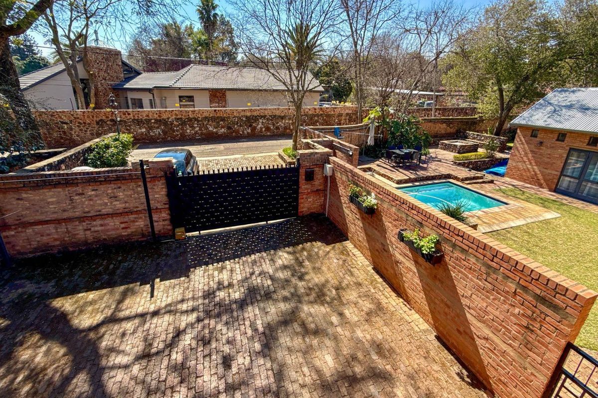 Aerial view of a property featuring a brick-paved driveway, secure metal gate, private swimming pool, and landscaped garden area.