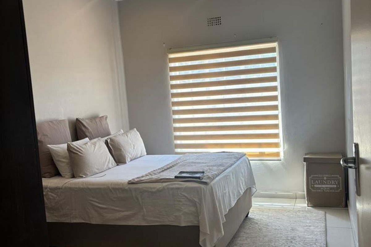 A well-maintained bedroom featuring neutral wall tones, tiled flooring, and a modern zebra-style roller blind on the window.