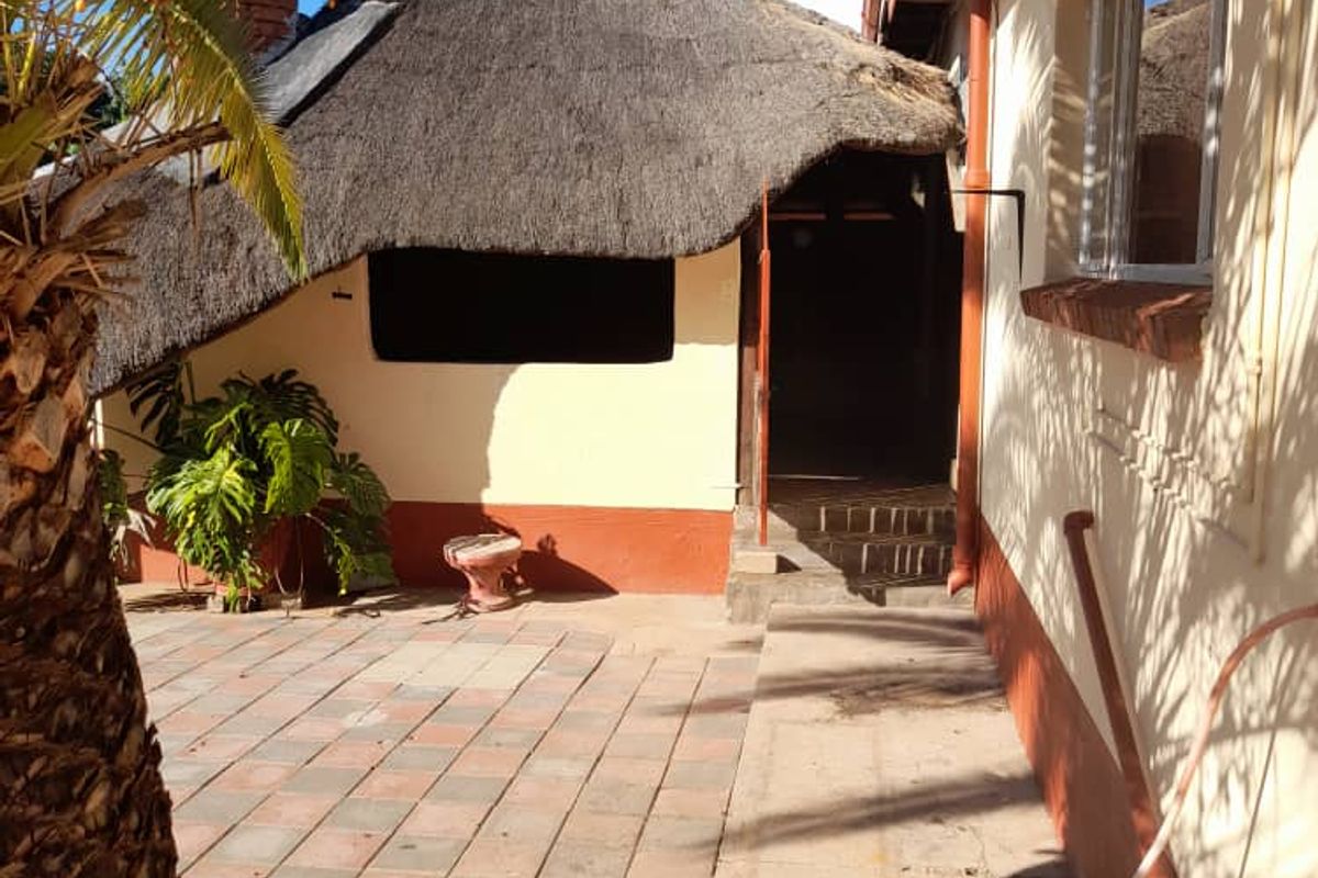 A rear courtyard area featuring a thatched roof structure, paved flooring, and direct access to the main house.