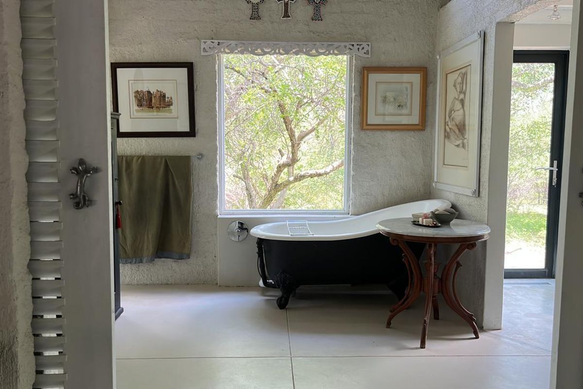A bright bathroom featuring a classic clawfoot bathtub positioned under a large window with views of the surrounding greenery.