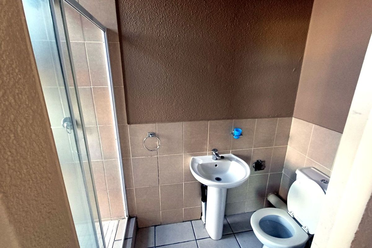 A functional bathroom featuring a pedestal washbasin, toilet, and a glass-enclosed shower with neutral wall and floor tiling.