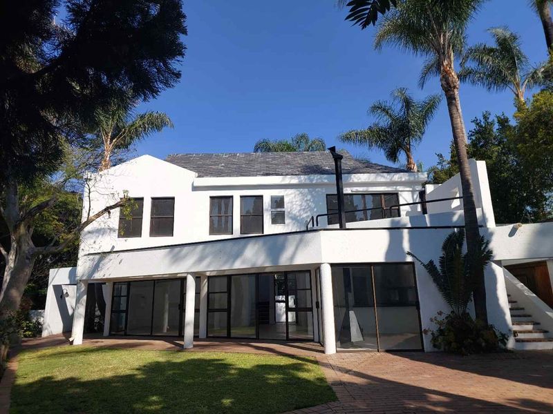 Rear view of a two-story cluster home featuring a paved patio, large sliding glass doors, a balcony, and an external staircase set in a garden.