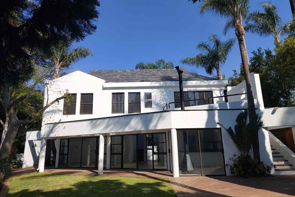 Rear view of a two-story cluster home featuring a paved patio, large sliding glass doors, a balcony, and an external staircase set in a garden.