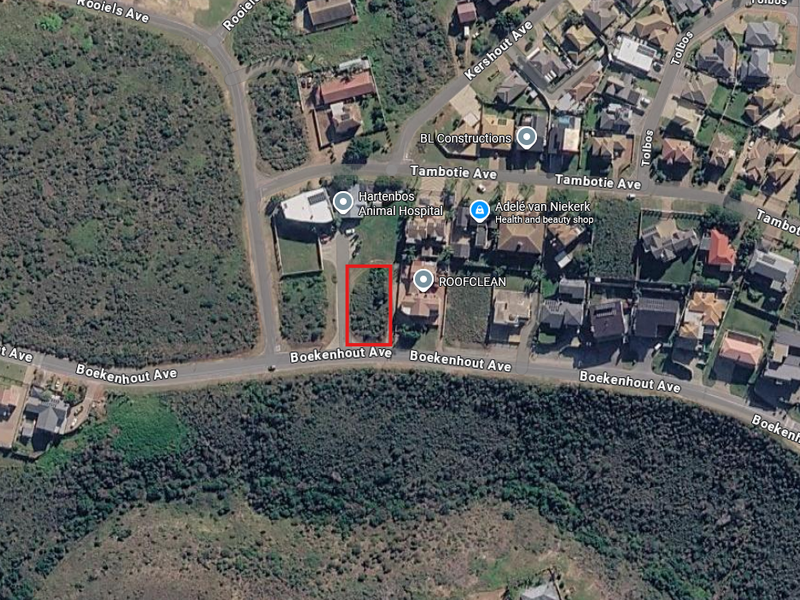 Aerial view of a vacant residential plot highlighted in red, situated in a developed suburban area near local amenities.