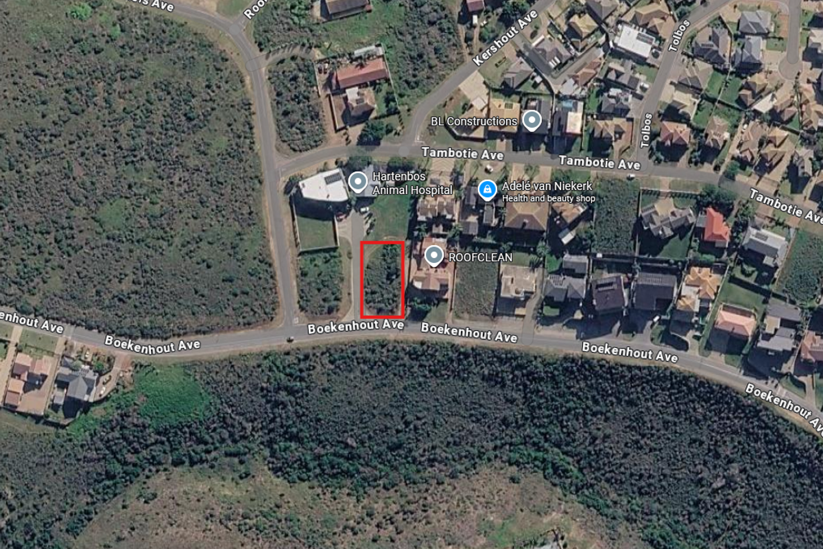 Aerial view of a vacant residential plot highlighted in red, situated in a developed suburban area near local amenities.