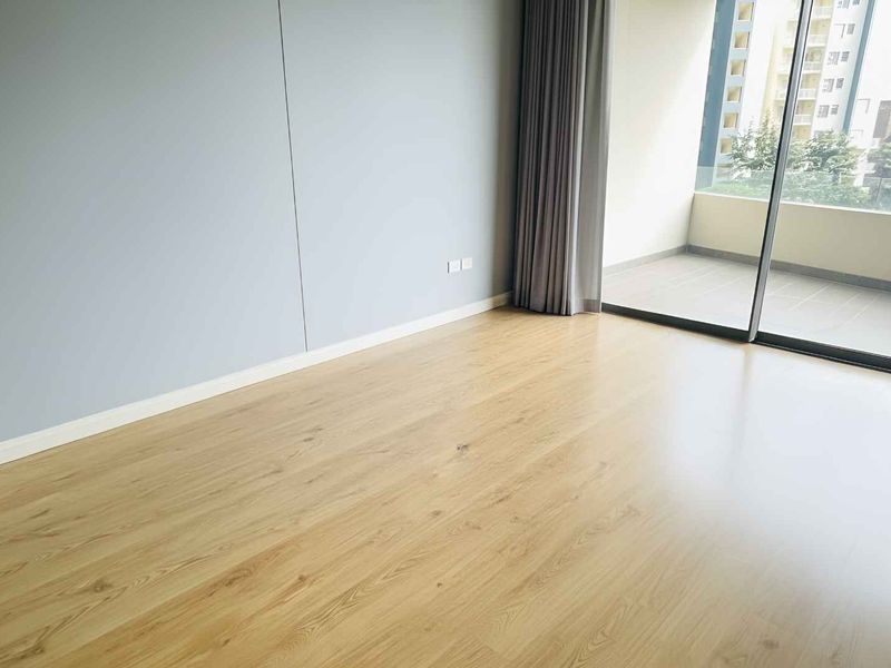 A bright, empty bedroom featuring modern laminate flooring, neutral wall finishes, and a large sliding glass door providing access to a private balcony.