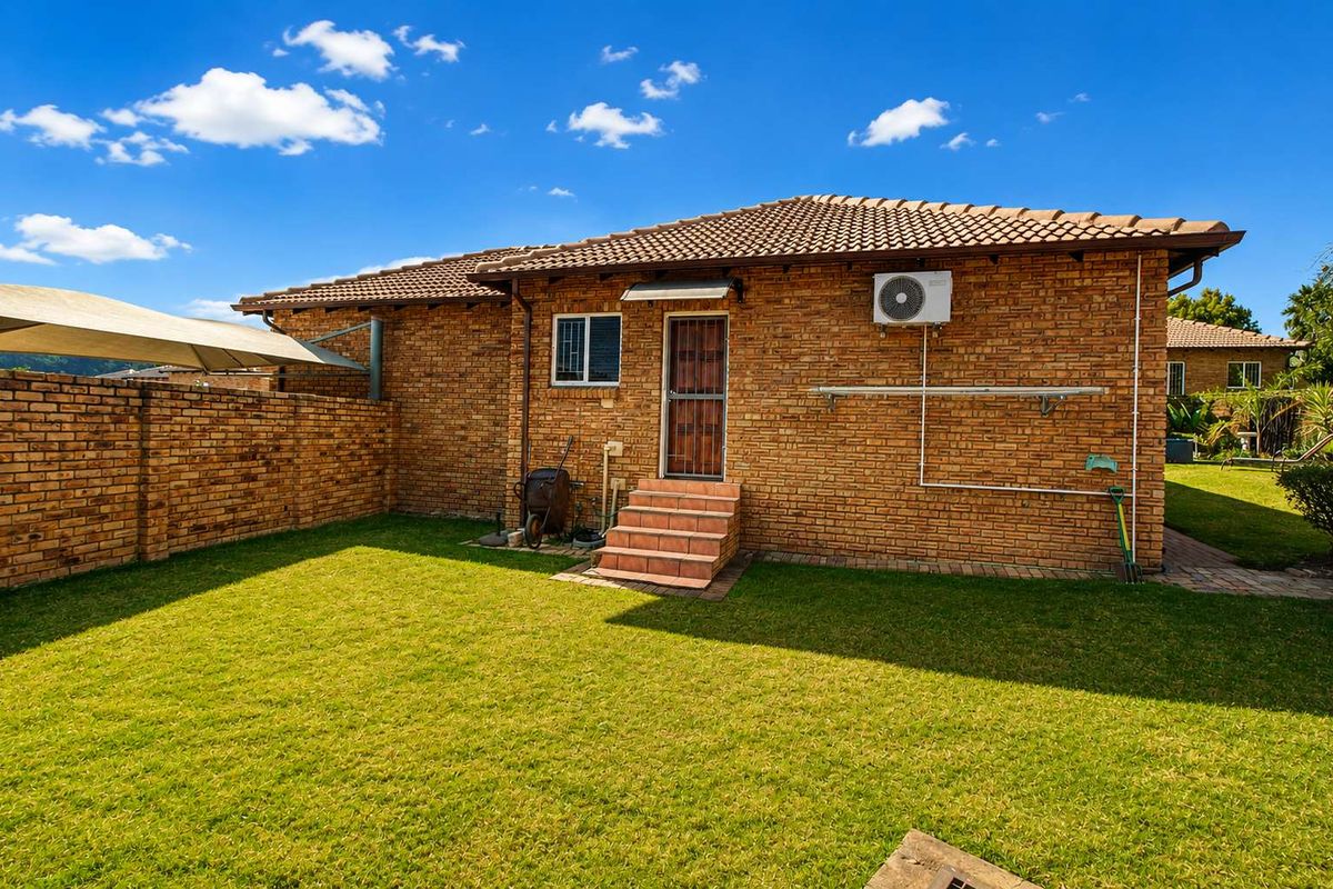 Rear view of the townhouse featuring a face brick facade, tiled roof, private garden, and secure access point.