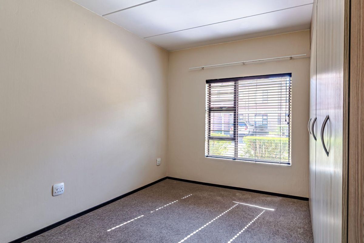 A clean, empty bedroom featuring neutral walls, carpeted flooring, and built-in cupboards with fitted venetian blinds.