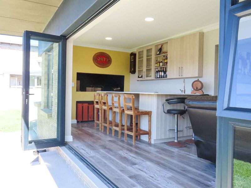 A modern indoor bar area featuring a built-in braai, custom cabinetry, and seamless access to the outdoor patio through large bi-fold doors.