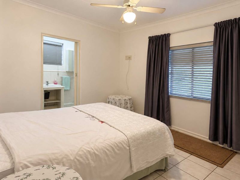 A bedroom featuring tiled flooring, a ceiling fan, and an en-suite bathroom, with natural light provided by a window with venetian blinds.
