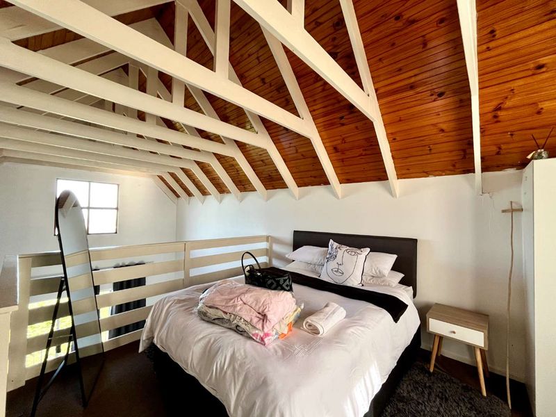 A loft-style bedroom featuring a vaulted timber ceiling with exposed white rafters and a mezzanine-style safety railing.