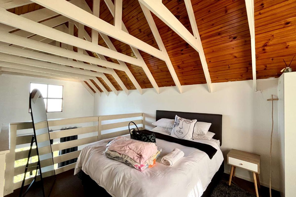 A loft-style bedroom featuring a vaulted timber ceiling with exposed white rafters and a mezzanine-style safety railing.