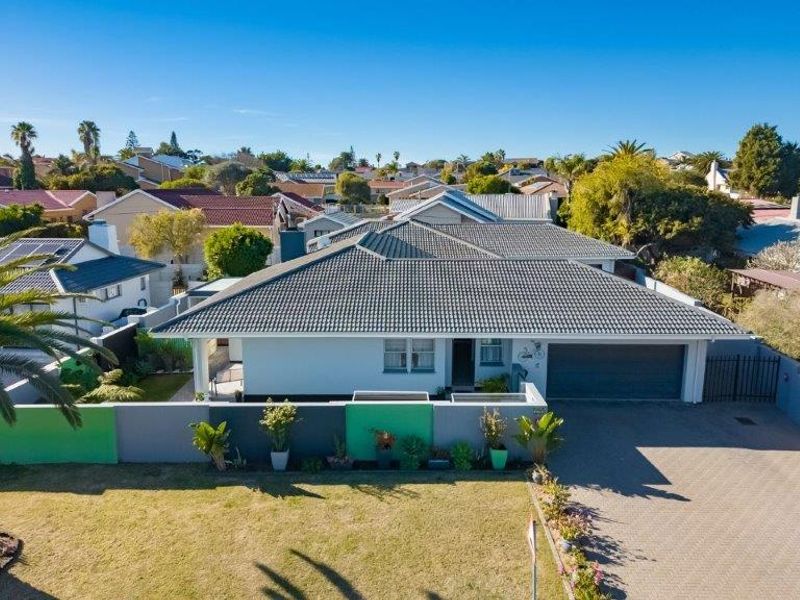 Aerial view of a well-maintained single-story house featuring a tiled roof, paved driveway, integrated garage, and a secure boundary wall in a residential neighborhood.