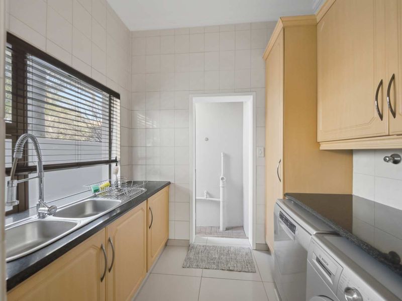 A functional laundry room featuring double stainless steel sinks, granite countertops, ample laminate cabinetry, and tiled finishes throughout.