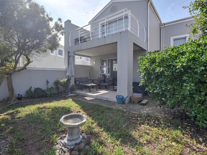 Rear view of the townhouse featuring a covered ground-floor patio, an upper-level balcony with railing, and a private garden area.