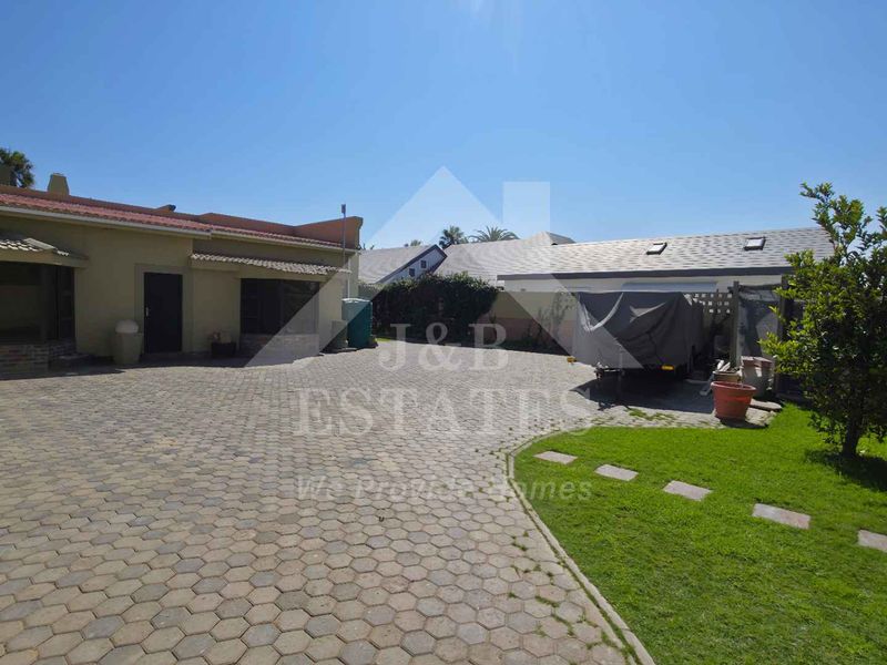 Rear exterior view of the property featuring a large paved driveway, lawn area, and boundary walling.