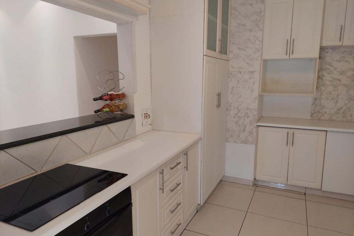A functional kitchen featuring white built-in cabinetry, stone countertops, an integrated electric hob and oven, and a convenient pass-through window to the living area.