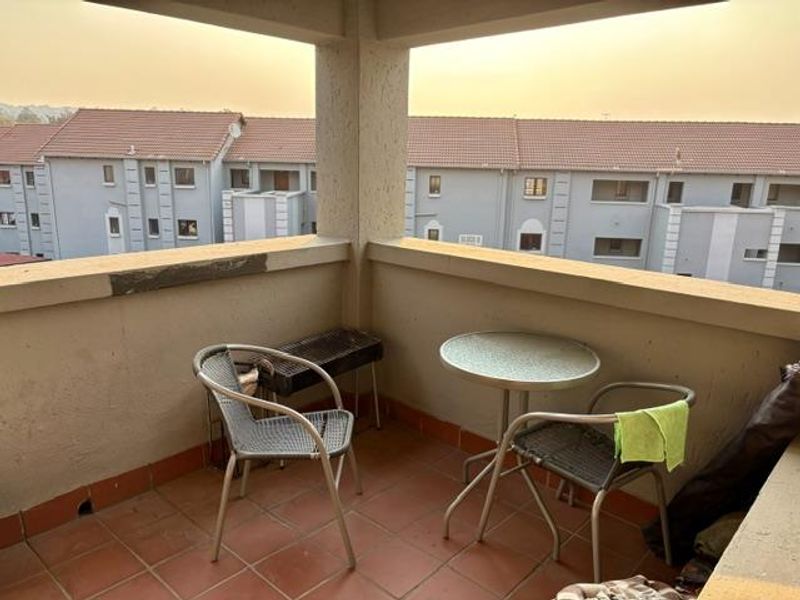 A covered balcony featuring tiled flooring and a concrete balustrade, offering an outdoor space with views of the surrounding apartment complex.