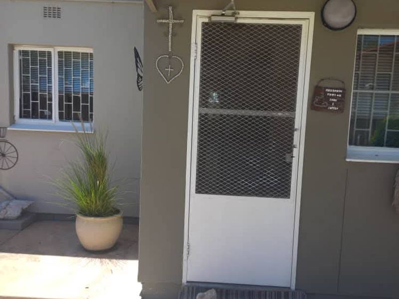 Front entrance area featuring a security gate, protective window bars, and a paved approach under a small structural awning.
