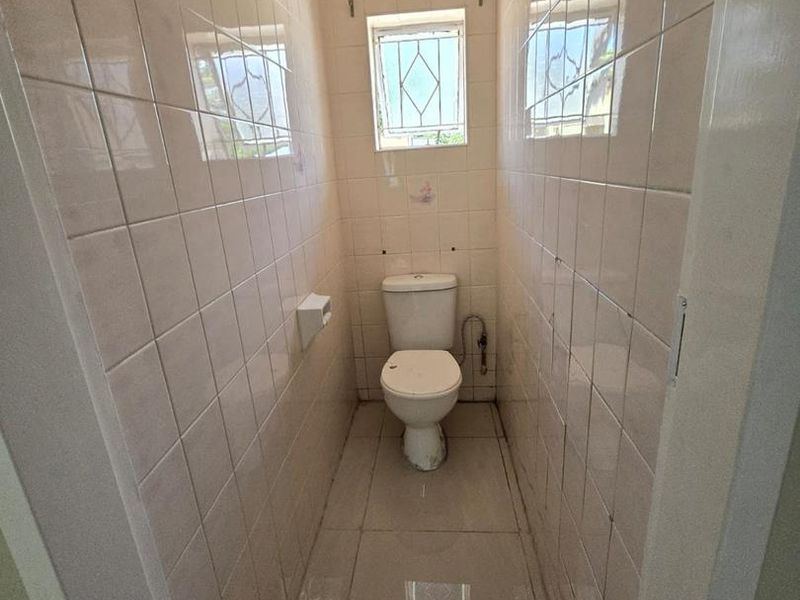 A compact, tiled guest toilet featuring a standard white toilet suite and a small window with security bars.