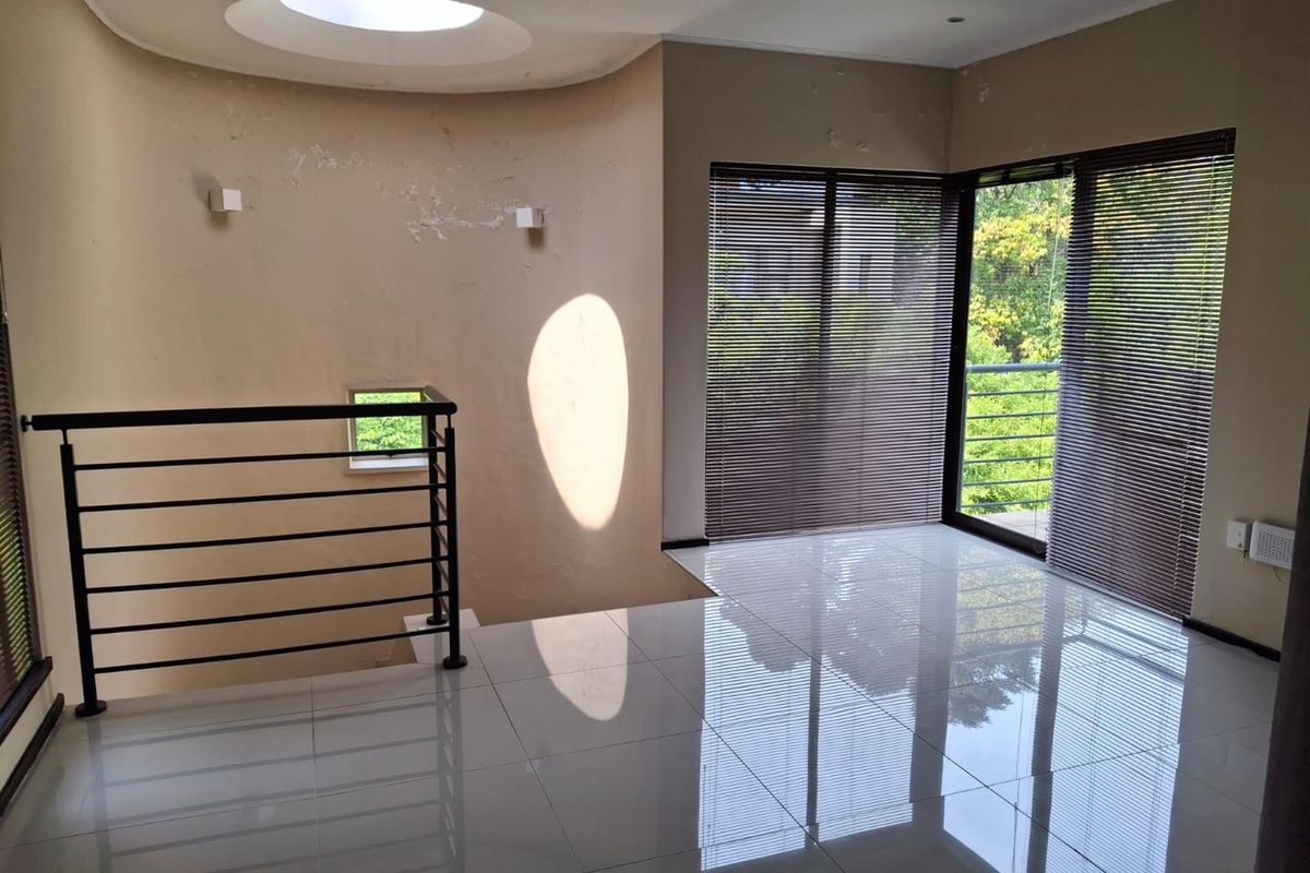 An empty living area featuring polished tile floors, a circular skylight, and a metal balustrade overlooking the lower level with large windows and blinds.