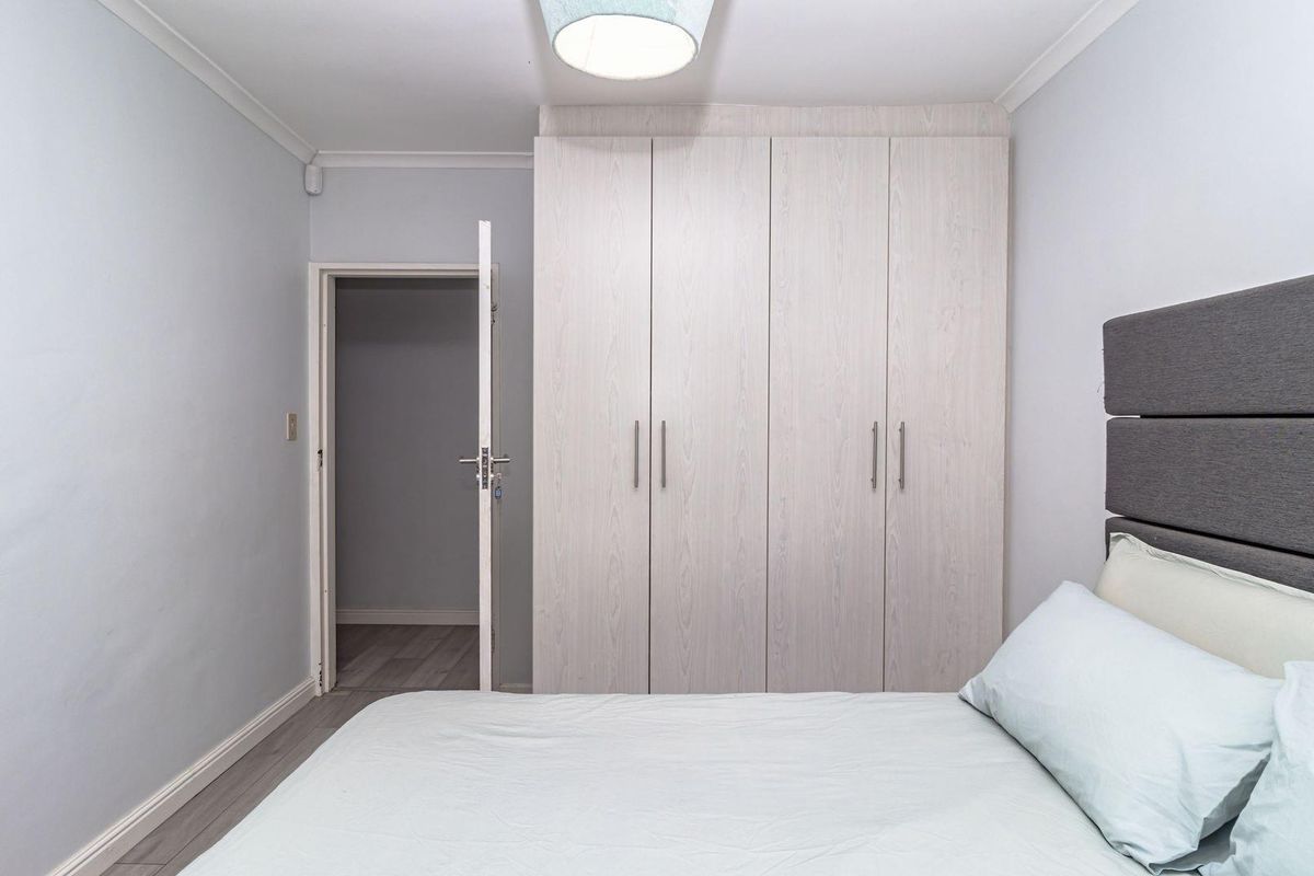 A well-maintained bedroom featuring built-in light wood-grain wardrobes and neutral wall finishes.