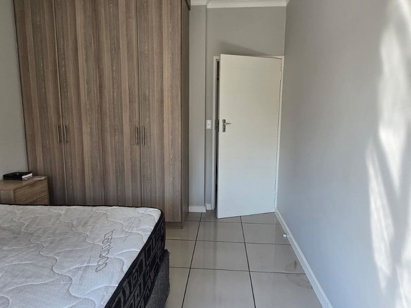 A bedroom featuring built-in wooden cupboards and neutral tiled flooring, offering a clean and functional space.