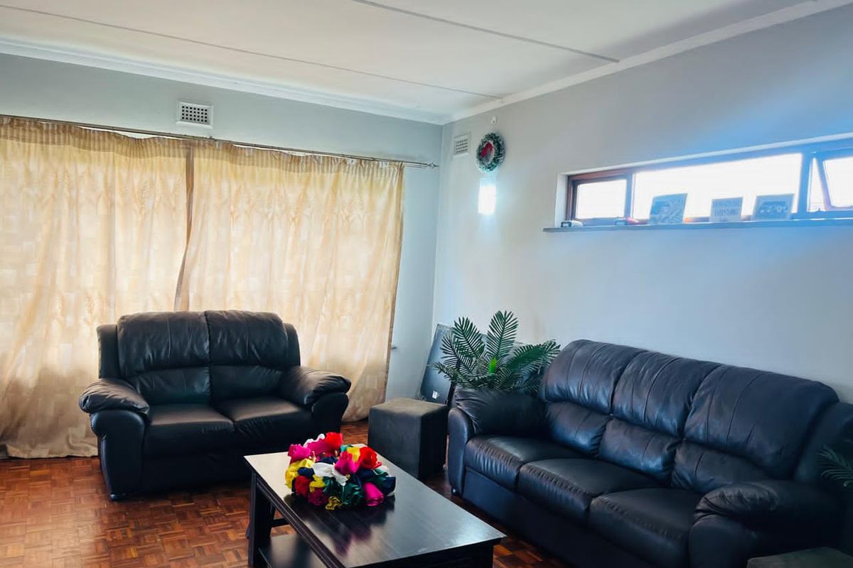 A living room featuring classic parquet flooring, neutral wall finishes, and natural light provided by top-hung windows.