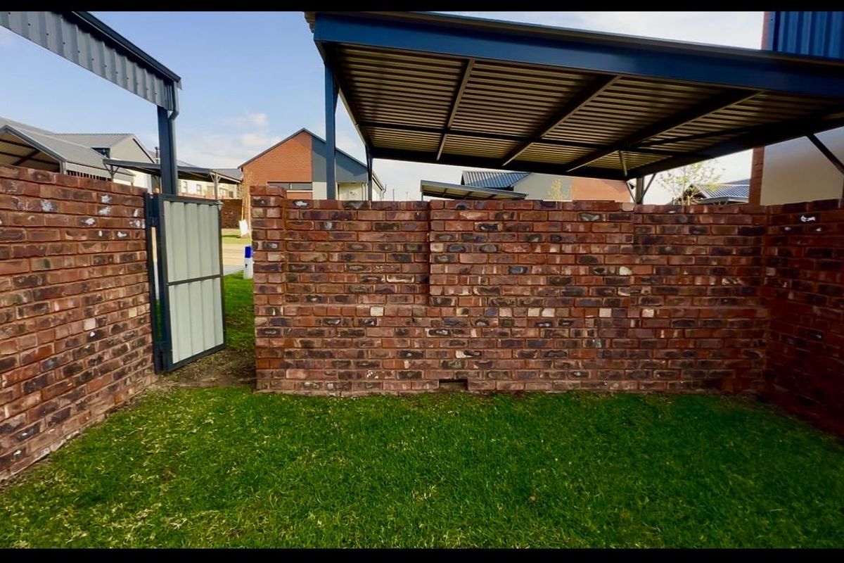 A private outdoor courtyard area featuring a brick boundary wall, a metal gate, and a covered carport structure.