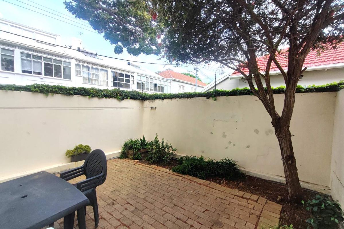 A private rear courtyard featuring brick paving, a mature tree, and a high boundary wall with some visible wear to the paint finish.