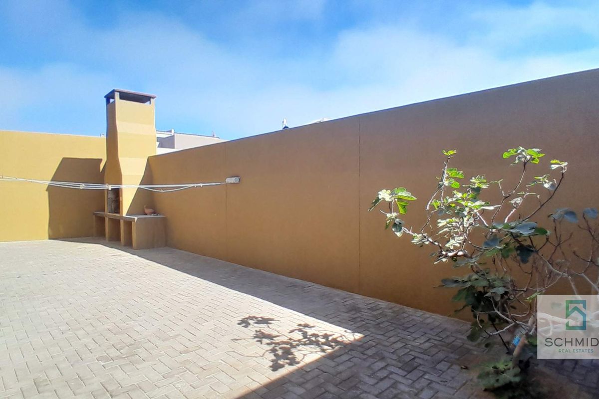 A private rear courtyard featuring a paved surface, high boundary walls, and a built-in braai area, ideal for outdoor entertaining.