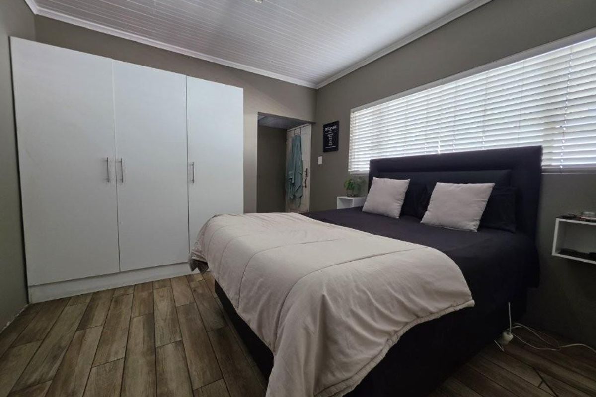 A well-maintained bedroom featuring built-in wardrobes, timber-look floor tiles, and a tongue and groove ceiling with venetian blinds.