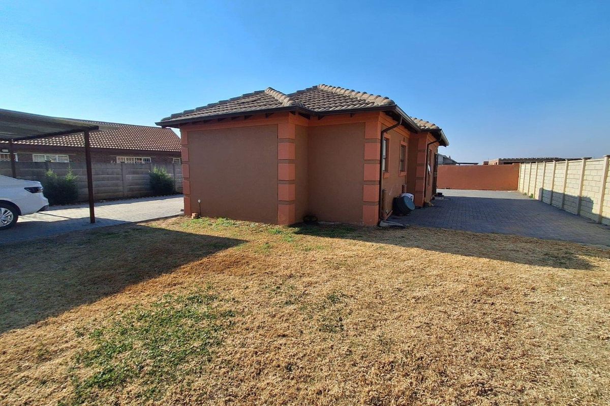 Rear view of the property featuring a paved driveway, carport, and a large garden area enclosed by precast concrete boundary walls.