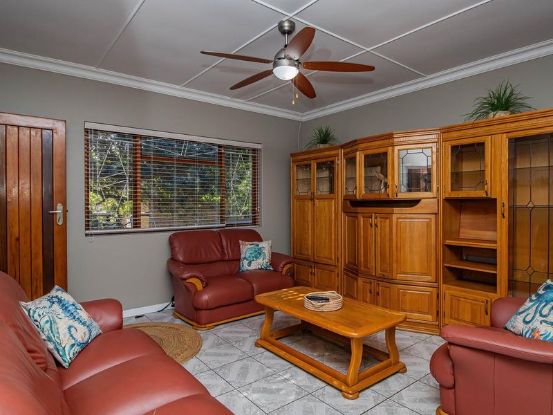 A living room featuring tiled flooring, a ceiling fan, and crown molding, providing a functional space with neutral wall tones.