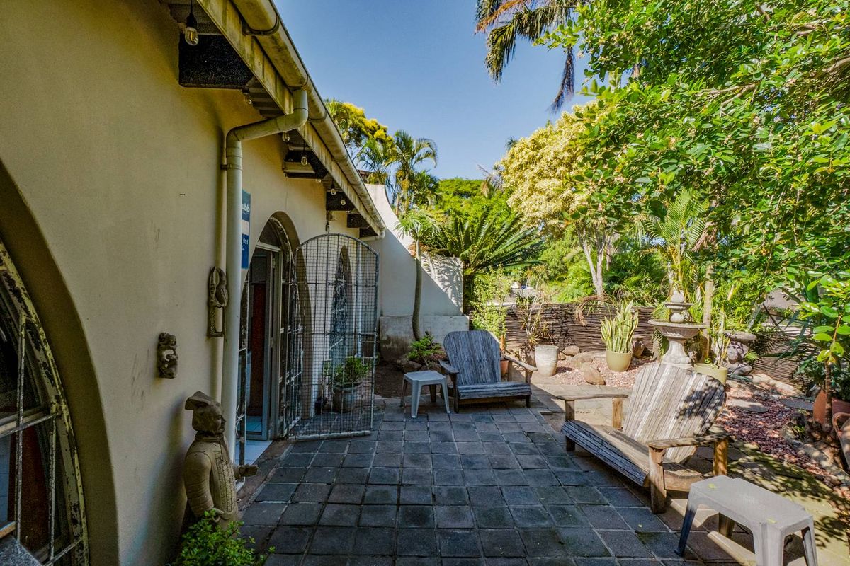A private rear patio area featuring paved flooring, arched doorways, and established garden surroundings, offering a quiet outdoor space for relaxation.