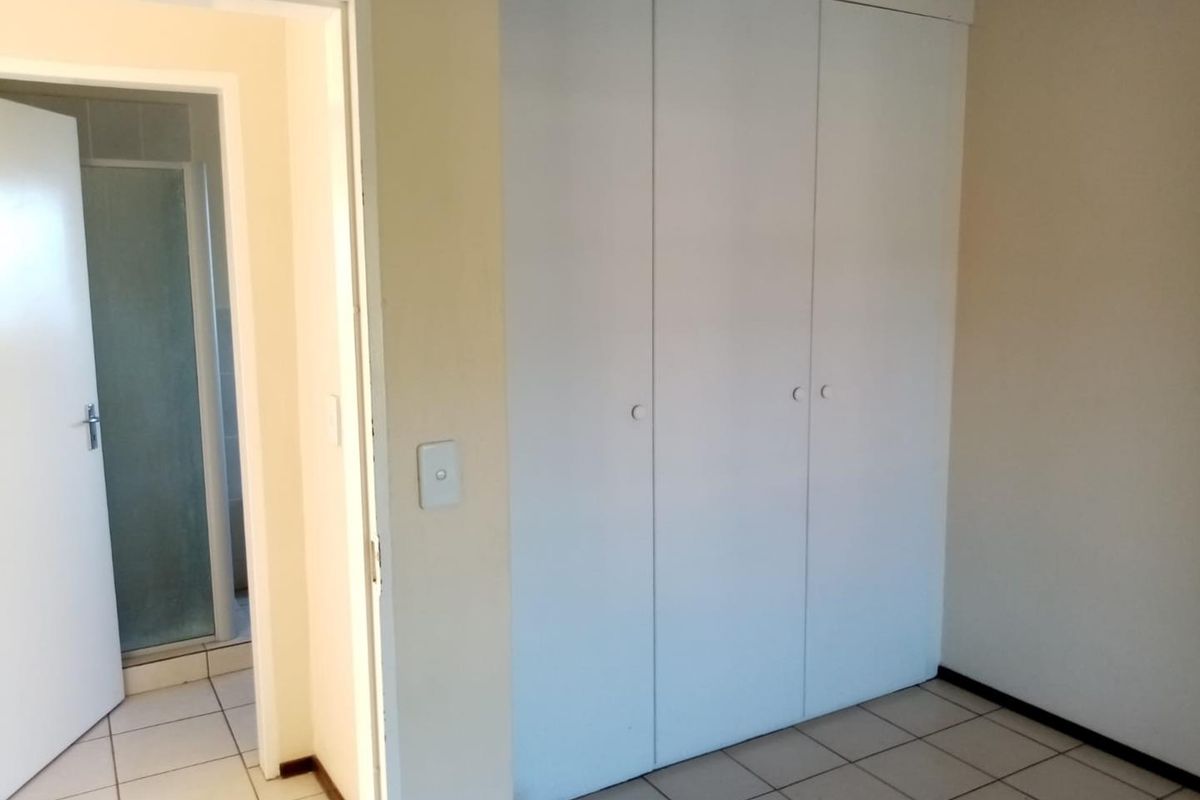 A clean, empty bedroom featuring built-in cupboards, tiled flooring, and direct access to an adjacent bathroom.