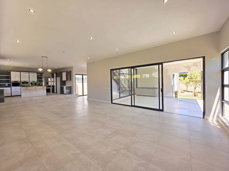 Spacious open-plan living area featuring large format floor tiles, recessed lighting, and a modern kitchen, seamlessly connecting to an outdoor patio through sliding glass doors.