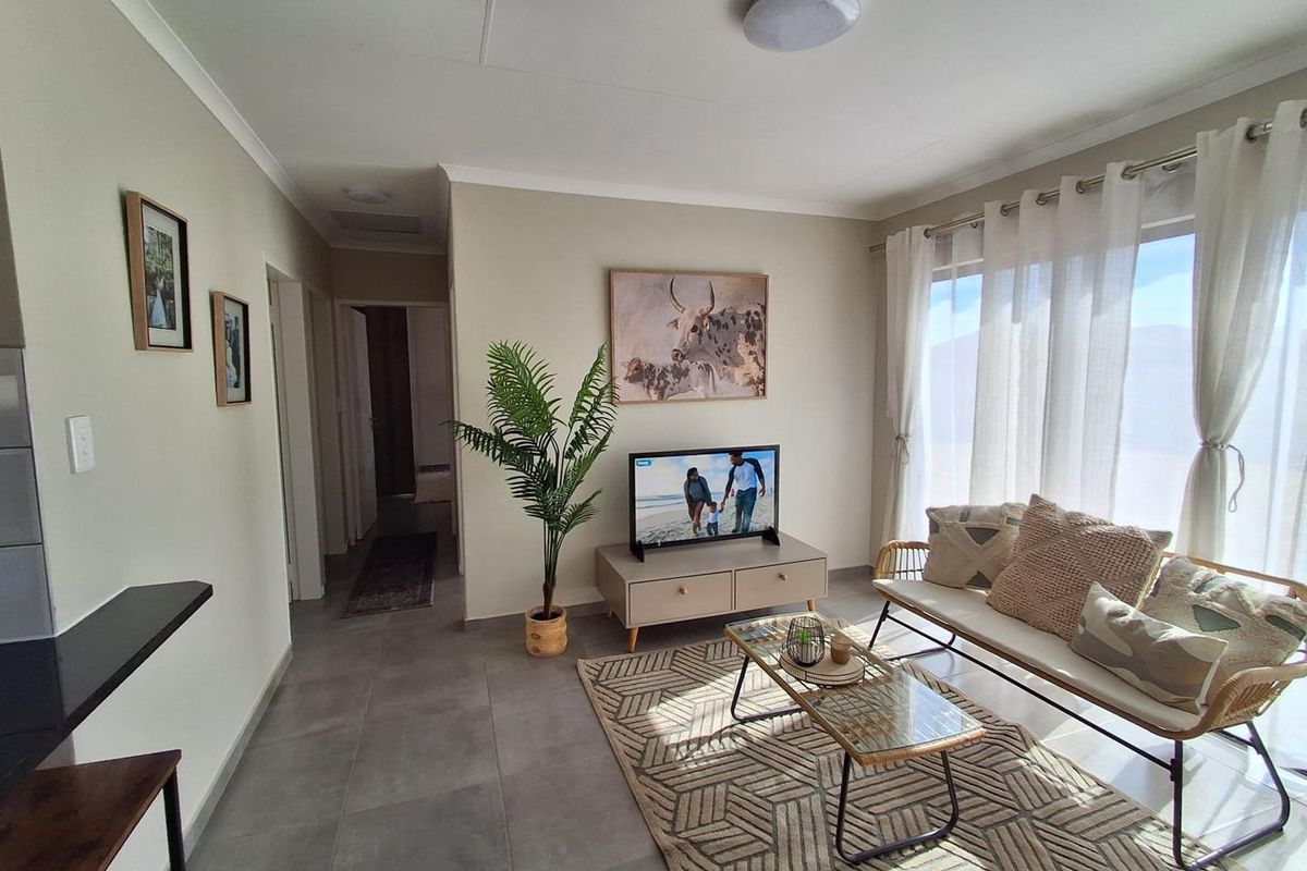 A bright and well-maintained living room featuring neutral wall tones, modern tiled flooring, and natural light through large windows.