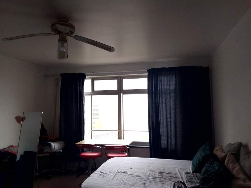 A bedroom featuring a ceiling fan and a large window that provides natural light.
