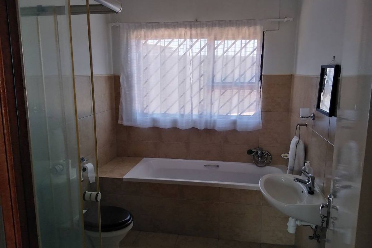A functional bathroom featuring a built-in bathtub, a separate shower enclosure, a pedestal basin, and tiled wall finishes.