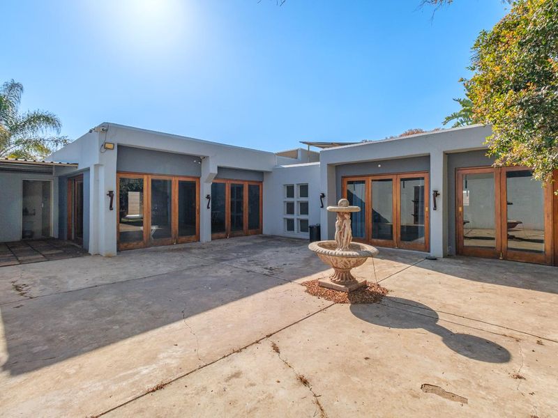 A spacious rear courtyard featuring concrete paving, a central stone fountain, and multiple timber-framed glass doors providing access to the home.
