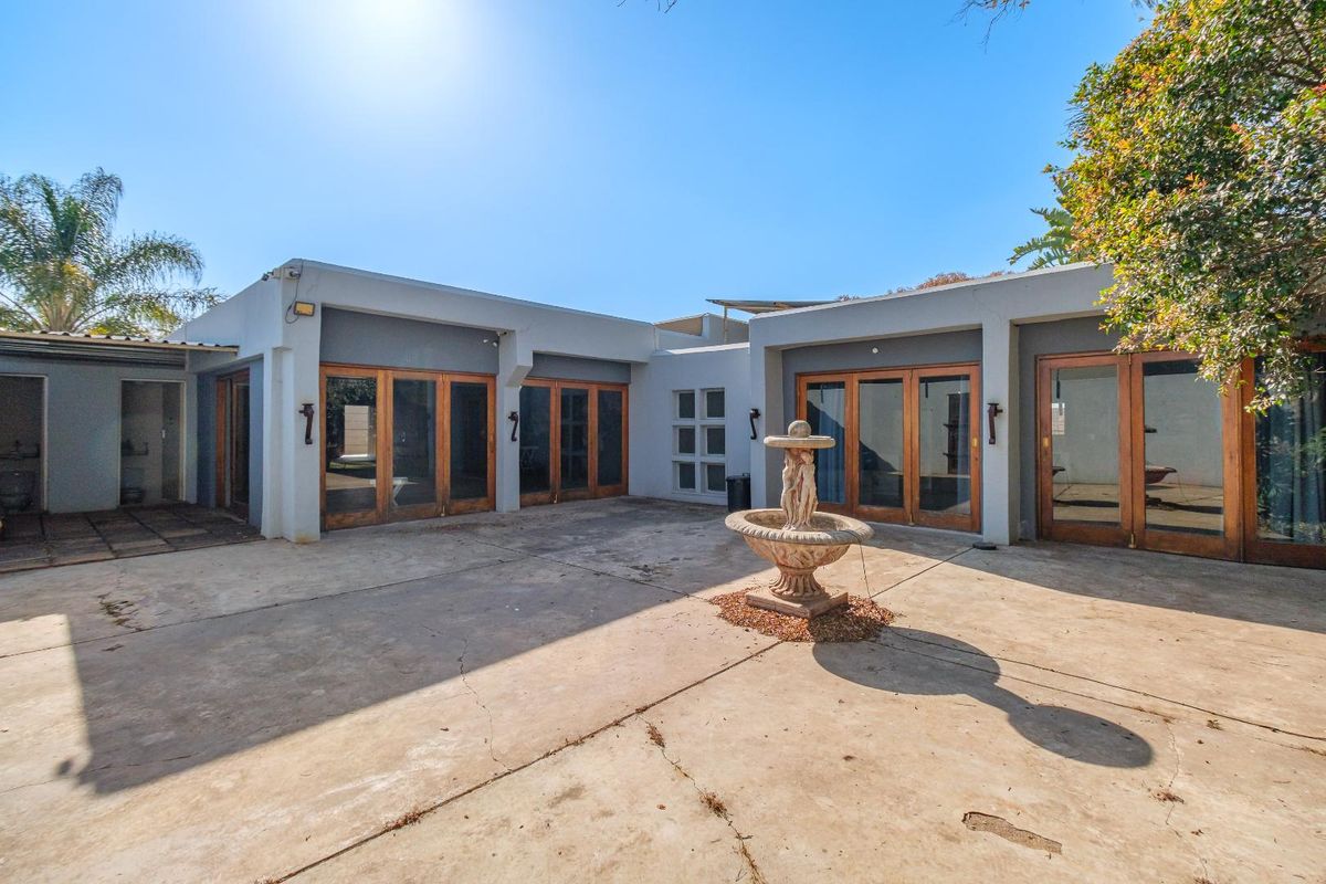 A spacious rear courtyard featuring concrete paving, a central stone fountain, and multiple timber-framed glass doors providing access to the home.
