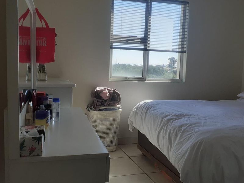 A functional bedroom featuring tiled flooring and a window with venetian blinds, offering natural light and a view.