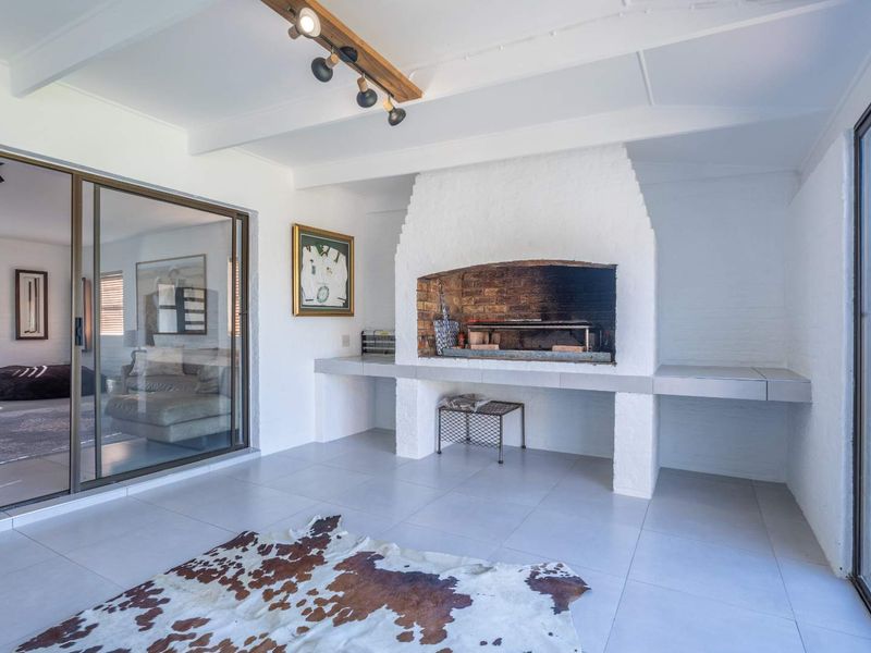 Covered patio area featuring a built-in brick braai, large sliding glass doors, and modern tiled flooring, offering a seamless transition to outdoor living.