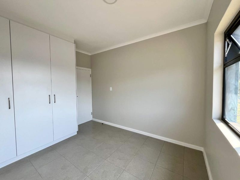 A clean, empty bedroom featuring neutral tiled flooring, built-in cupboards, and a modern aluminium window frame.