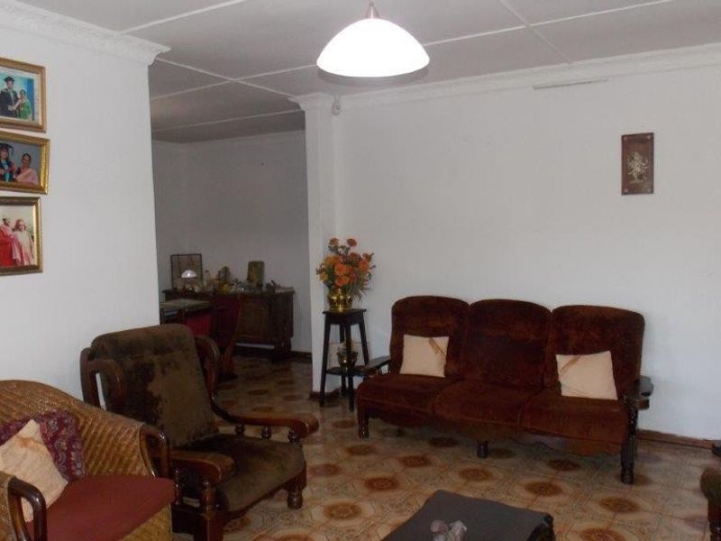 A living room featuring tiled flooring and decorative ceiling cornicing, offering a dated interior space ready for modernization.