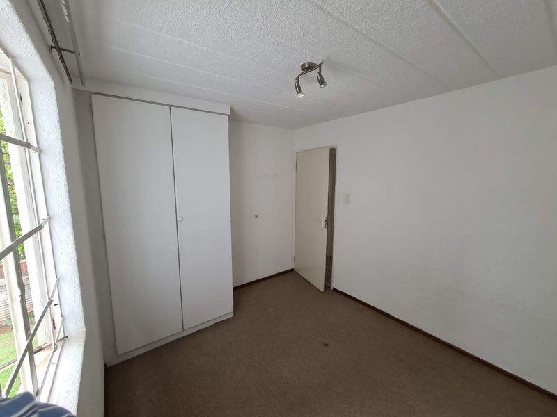 An empty bedroom featuring a built-in wardrobe, carpeted flooring, and a textured ceiling, offering a blank canvas for personalization.