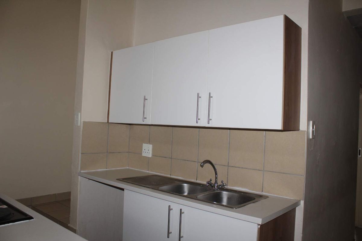 A clean and functional kitchen area featuring white built-in cabinetry, a double bowl stainless steel sink, and neutral tiled splashbacks.