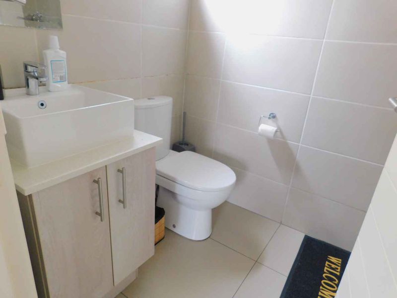 Compact bathroom featuring a modern vessel sink on a vanity cabinet, white toilet, and neutral wall and floor tiling.