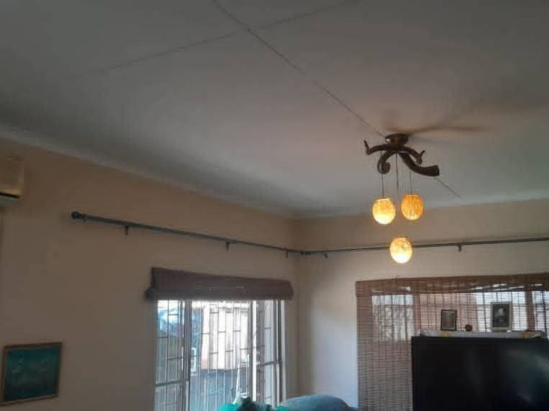 A living room featuring a ceiling fan, wall-mounted air conditioning unit, and security bars on the windows.